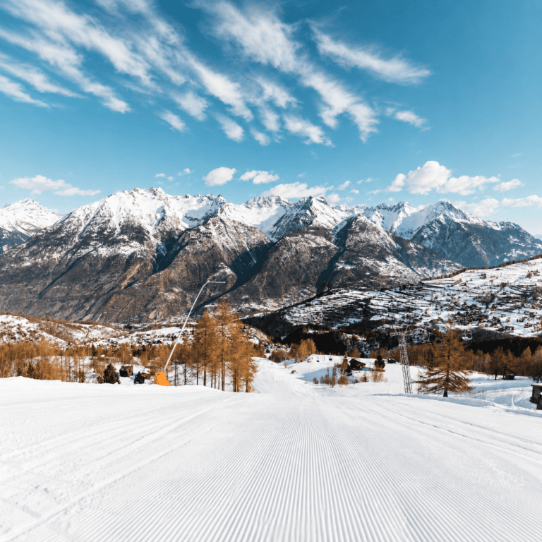 Gepflegte Skipiste vor verschneiten Alpen